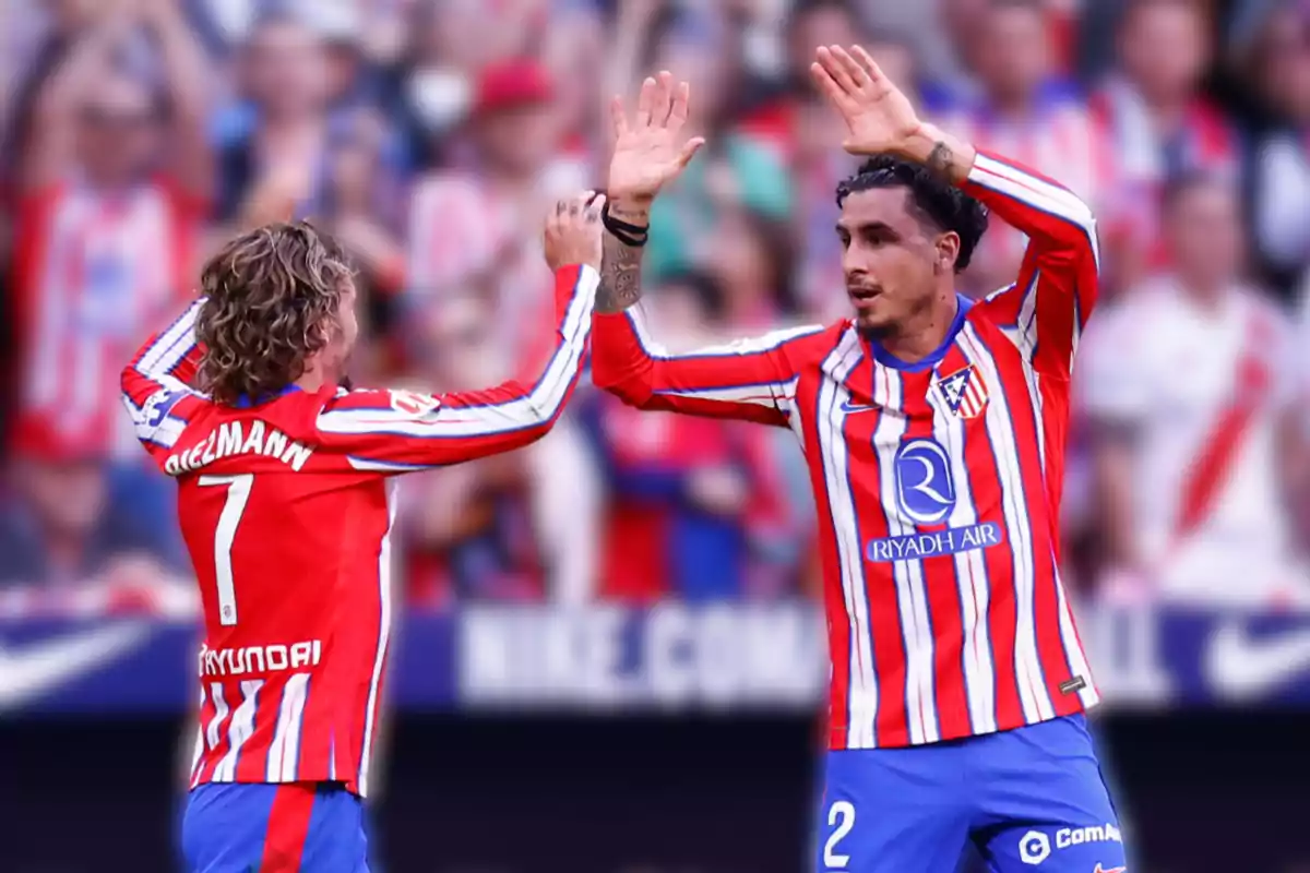 Dos jugadores de fútbol del Atlético de Madrid celebran en el campo con camisetas a rayas rojas y blancas.