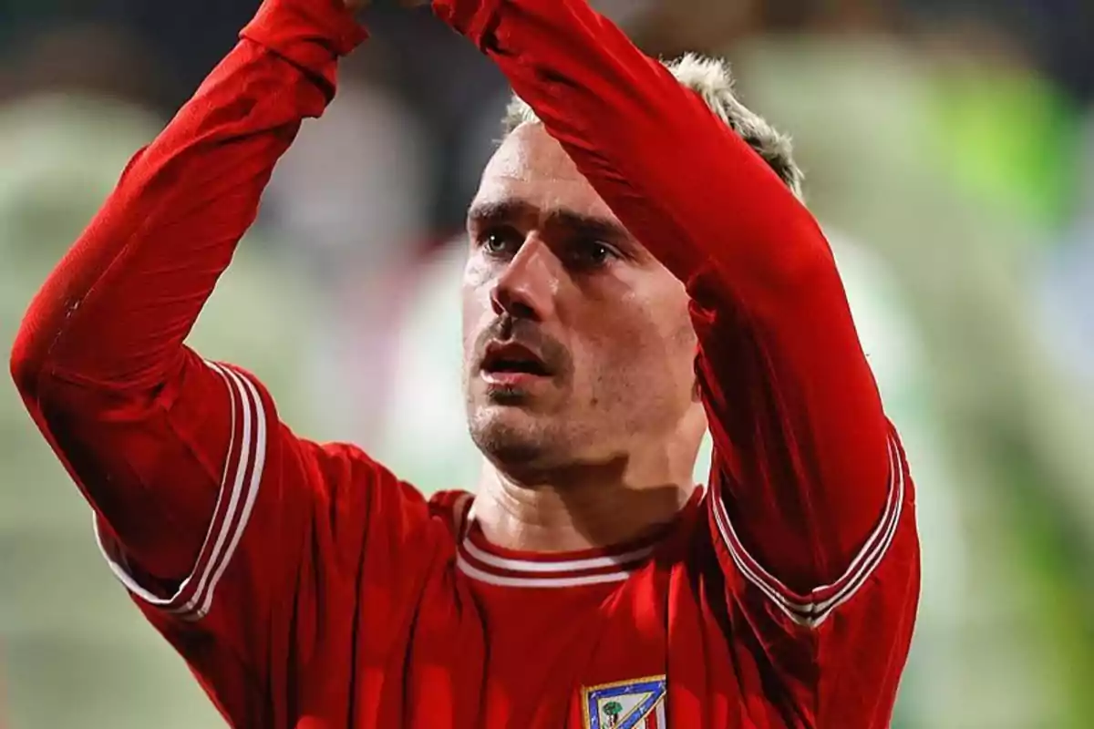 Jugador de fútbol con camiseta roja levantando los brazos.