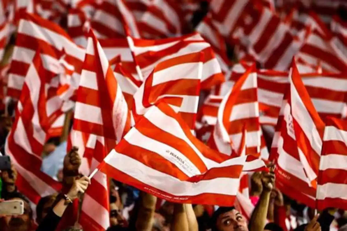 Personas ondeando banderas rojas y blancas en un evento deportivo.