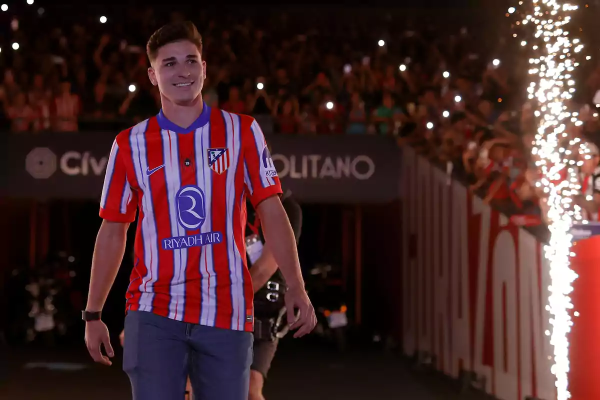 A football player wearing an Atlético de Madrid shirt is presented in a stadium full of fans as he walks down a catwalk illuminated with fireworks. A football player wearing an Atlético de Madrid shirt is presented in a stadium full of fans as he walks down a catwalk illuminated with fireworks.