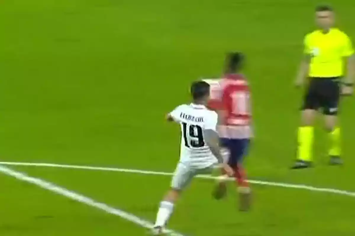 A soccer player with the number 19 on his jersey is in action during a match, while a referee and another player are visible in the background. A soccer player with the number 19 on his jersey is in action during a match, while a referee and another player are visible in the background.