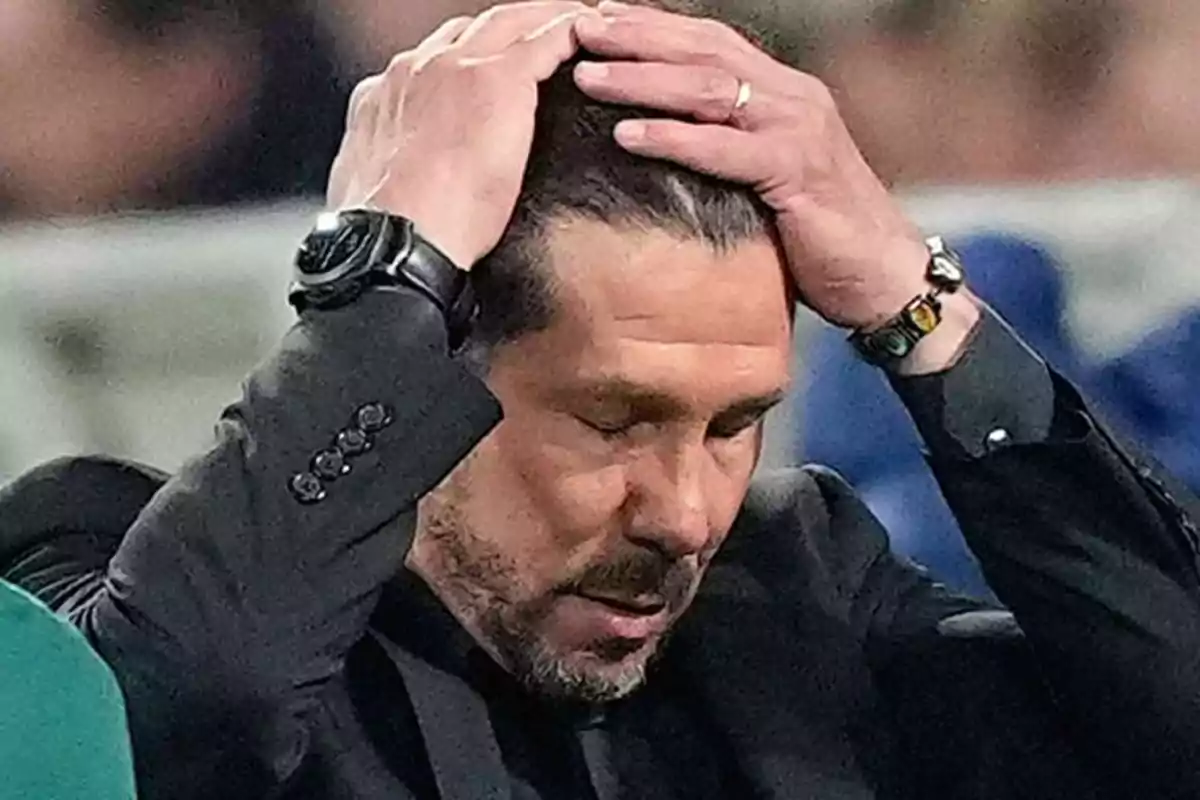 Man in black suit puts his hands on his head with a worried expression.