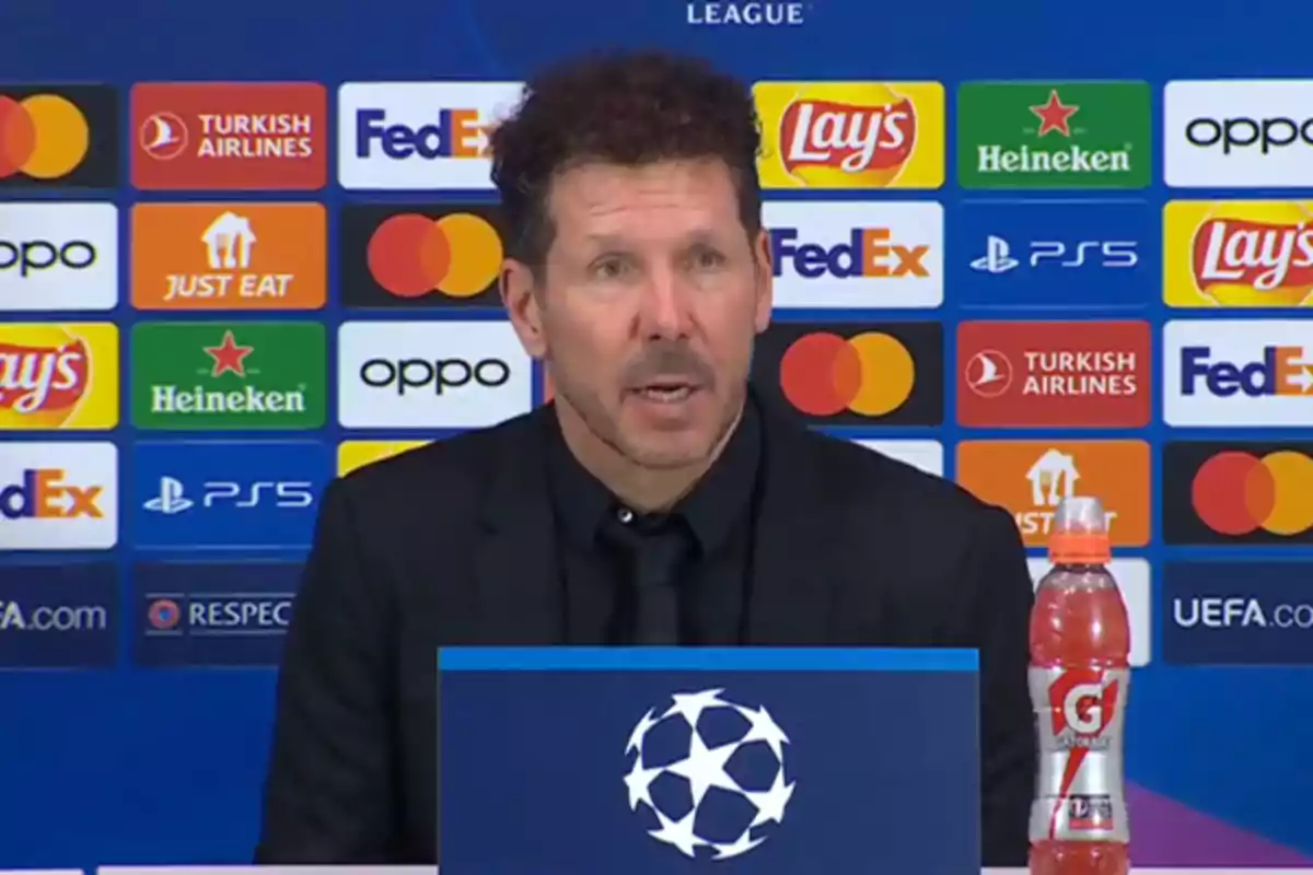 Un hombre hablando en una conferencia de prensa de la UEFA Champions League con varios logotipos de patrocinadores en el fondo.