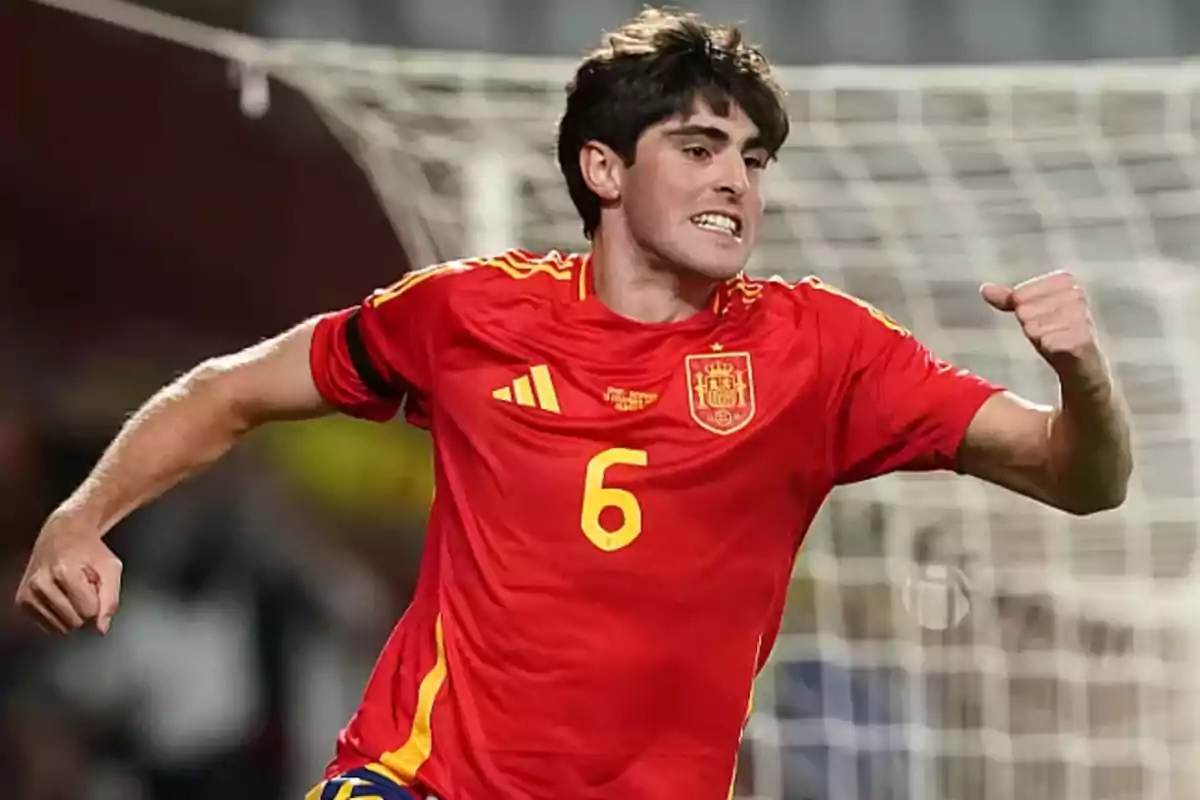 Jugador de fútbol con la camiseta roja de España celebrando un gol frente a la portería.