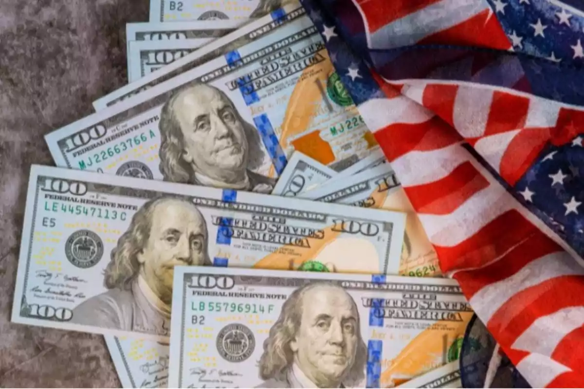 Billetes de cien dólares estadounidenses junto a una bandera de Estados Unidos