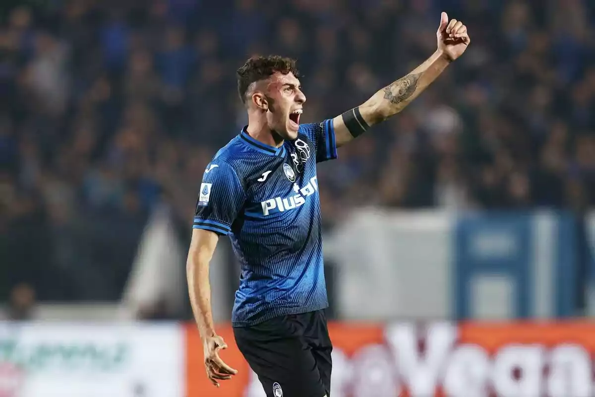 Futbolista con uniforme azul y negro celebrando en la cancha con el brazo derecho levantado y el pulgar hacia arriba Futbolista con uniforme azul y negro celebrando en la cancha con el brazo derecho levantado y el pulgar hacia arriba