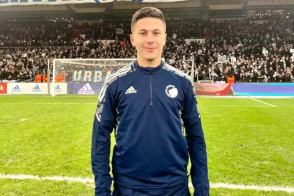 Joven con uniforme deportivo azul posando en un estadio de fútbol lleno de espectadores Joven con uniforme deportivo azul posando en un estadio de fútbol lleno de espectadores