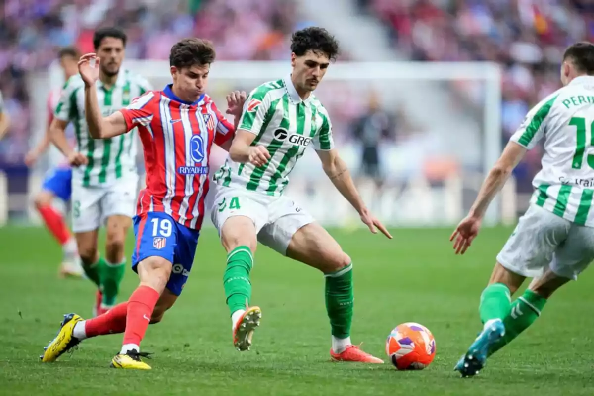 Dos futbolistas disputan el balón durante un partido mientras otros jugadores observan la jugada en el campo. Dos futbolistas disputan el balón durante un partido mientras otros jugadores observan la jugada en el campo.