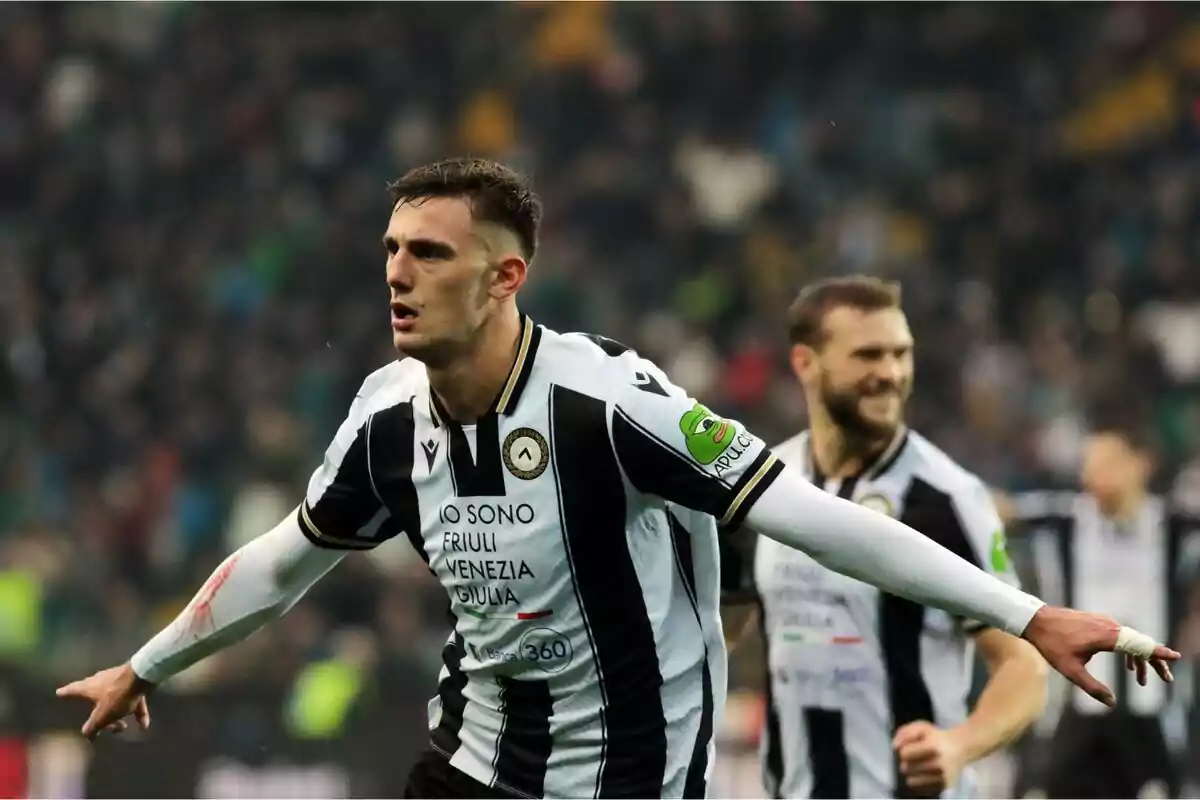 Futbolista del Udinese celebrando un gol con los brazos extendidos mientras otro compañero sonríe al fondo Futbolista del Udinese celebrando un gol con los brazos extendidos mientras otro compañero sonríe al fondo