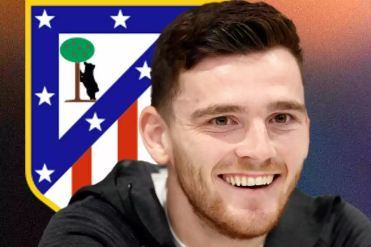 Un hombre sonriente en primer plano con el escudo del Atlético de Madrid de fondo