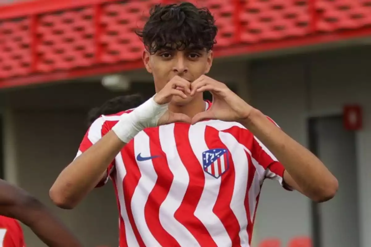 Joven futbolista con uniforme rojiblanco haciendo un gesto de corazón con las manos en el campo de juego Joven futbolista con uniforme rojiblanco haciendo un gesto de corazón con las manos en el campo de juego