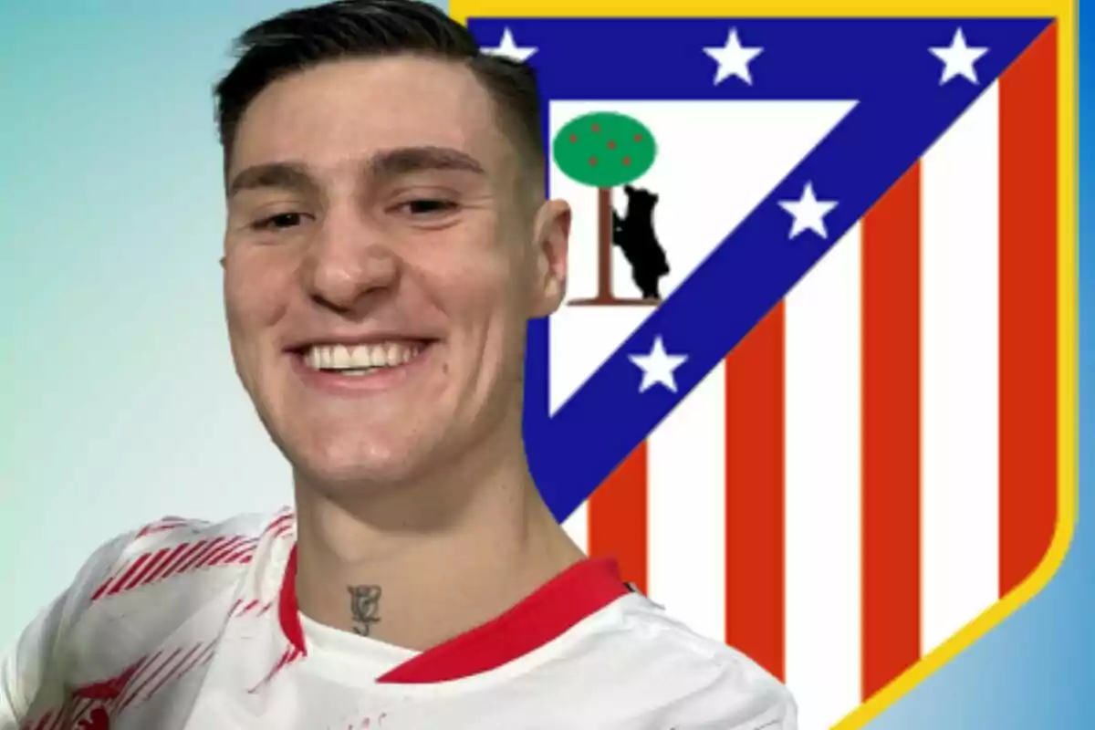 Un futbolista sonriente con una camiseta blanca y roja posando frente al escudo del Atlético de Madrid