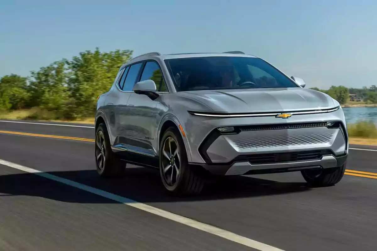 Silver Chevrolet SUV driving on a paved road alongside a natural landscape with trees and clear sky Silver Chevrolet SUV driving on a paved road alongside a natural landscape with trees and clear sky