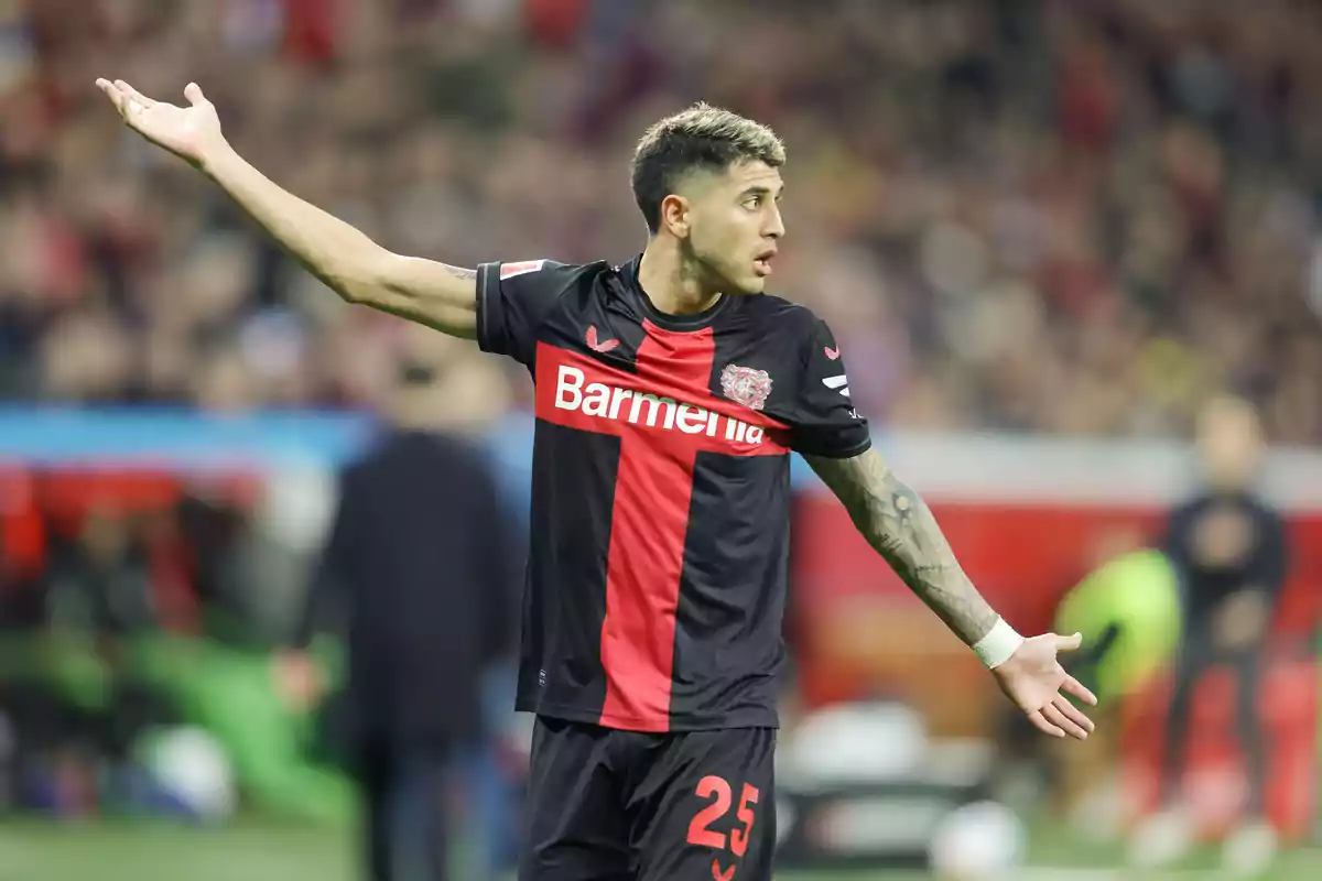 Futbolista del Bayer Leverkusen con el uniforme negro y rojo gesticulando con los brazos abiertos en el campo durante un partido