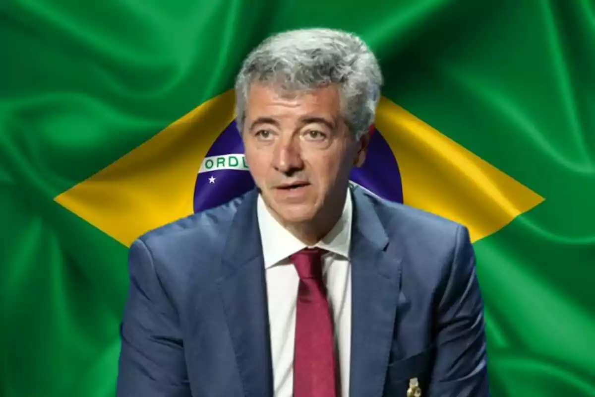 Hombre de cabello canoso con traje azul y corbata roja frente a una bandera de Brasil