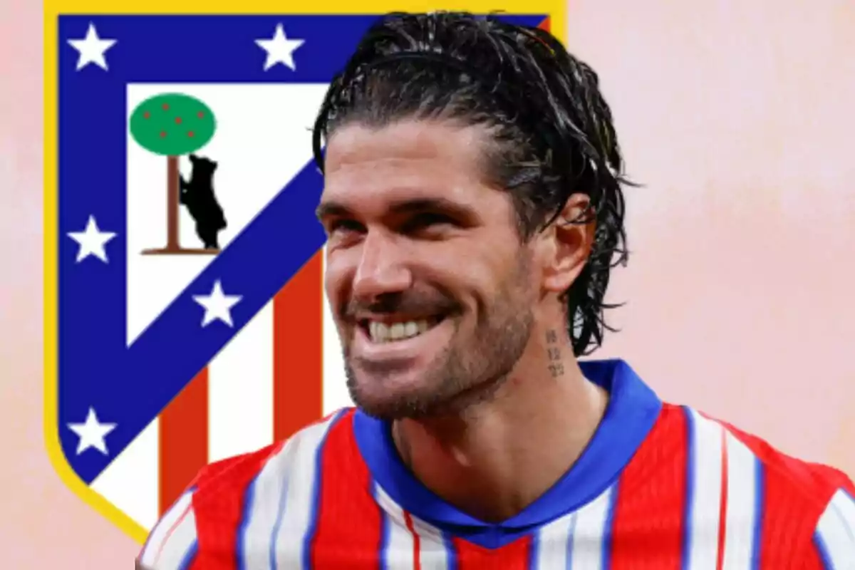 Futbolista sonriente con camiseta rojiblanca frente al escudo del Atlético de Madrid
