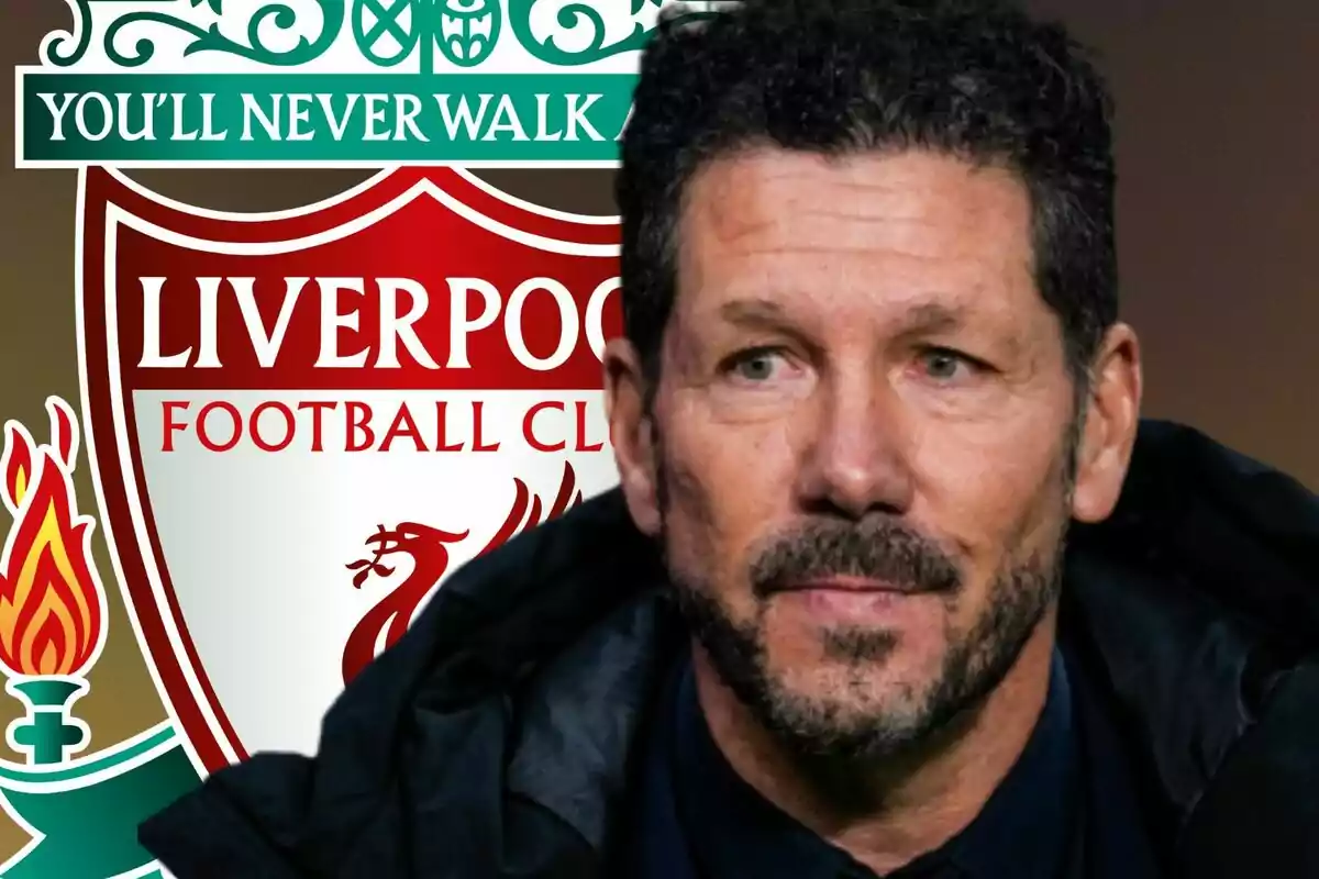 Un hombre de cabello rizado y barba frente al escudo del Liverpool Football Club