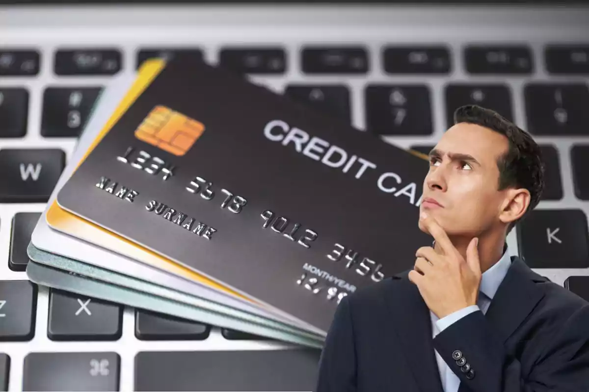 Hombre pensativo frente a varias tarjetas de crédito sobre un teclado de computadora