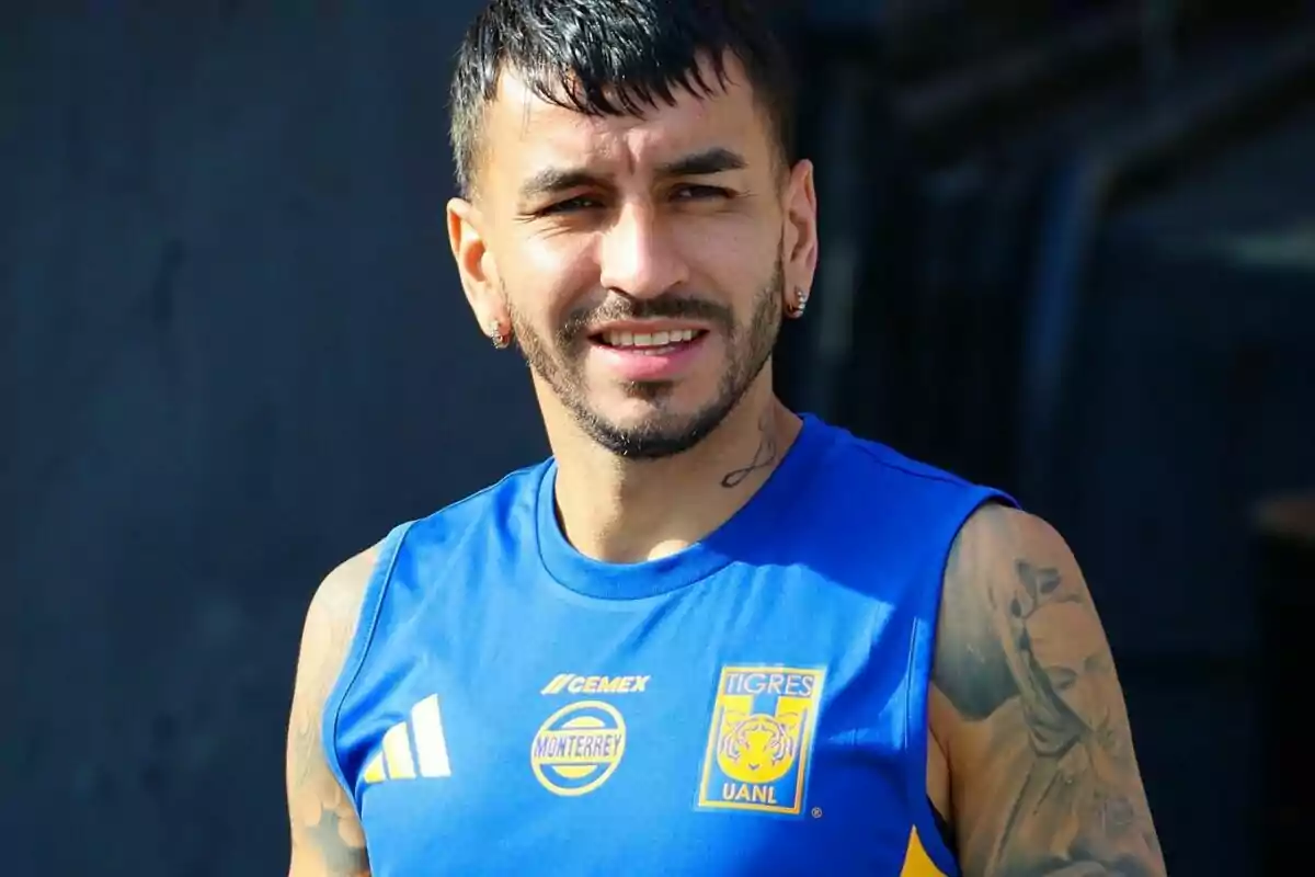 Jugador de fútbol con camiseta azul de Tigres UANL y varios tatuajes en los brazos, sonriendo al aire libre Jugador de fútbol con camiseta azul de Tigres UANL y varios tatuajes en los brazos, sonriendo al aire libre