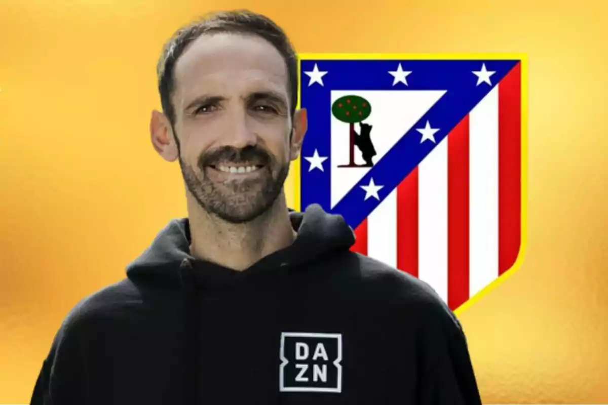 Hombre con sudadera negra de DAZN sonríe frente al escudo del Atlético de Madrid sobre un fondo amarillo