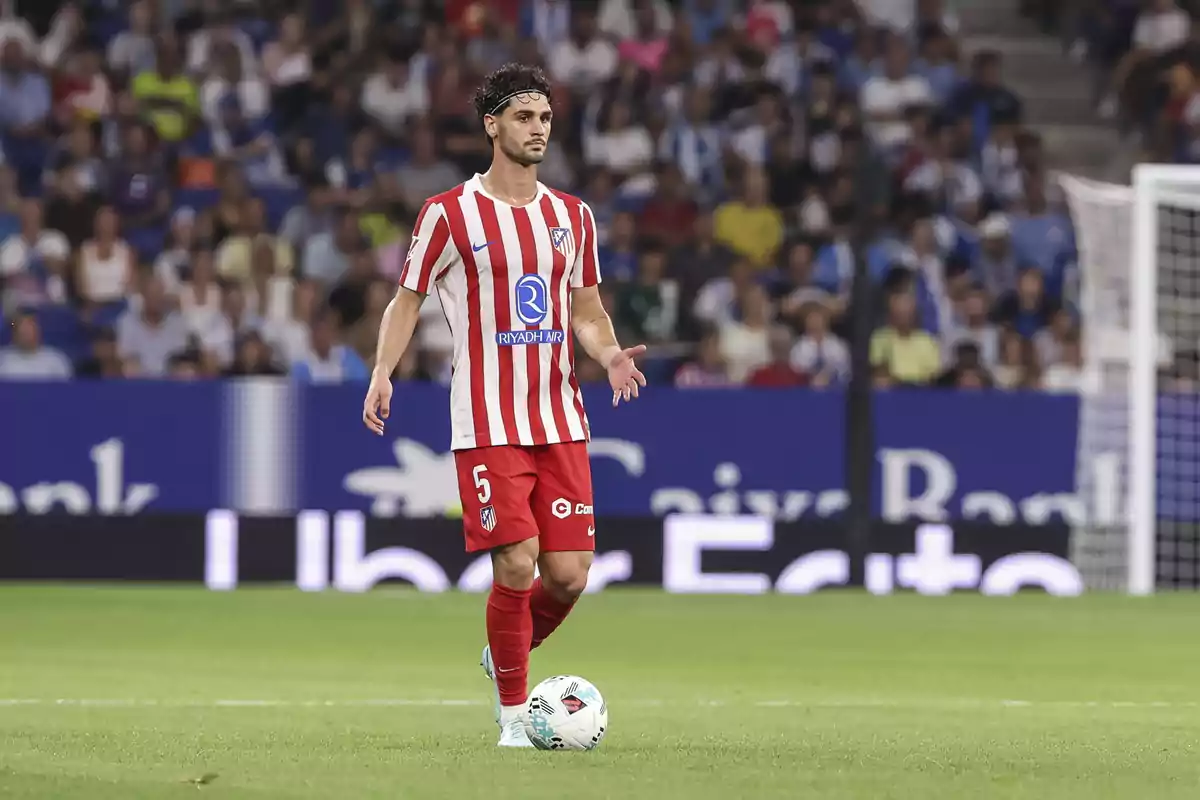 Futbolista del Atlético de Madrid con el número 5 en el uniforme, controlando el balón en un partido frente a una multitud en el estadio Futbolista del Atlético de Madrid con el número 5 en el uniforme, controlando el balón en un partido frente a una multitud en el estadio