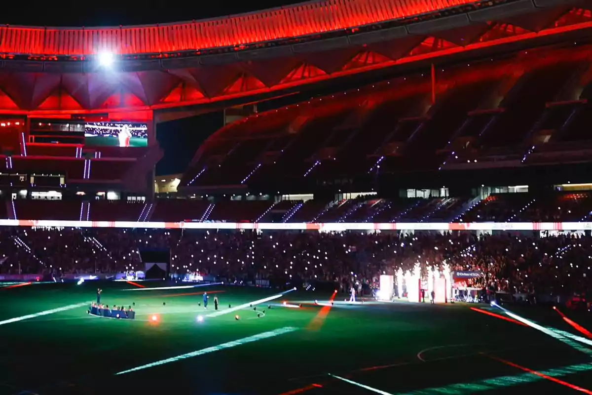 Estadio iluminado durante un evento nocturno con luces rojas y público usando linternas de sus teléfonos móviles Estadio iluminado durante un evento nocturno con luces rojas y público usando linternas de sus teléfonos móviles