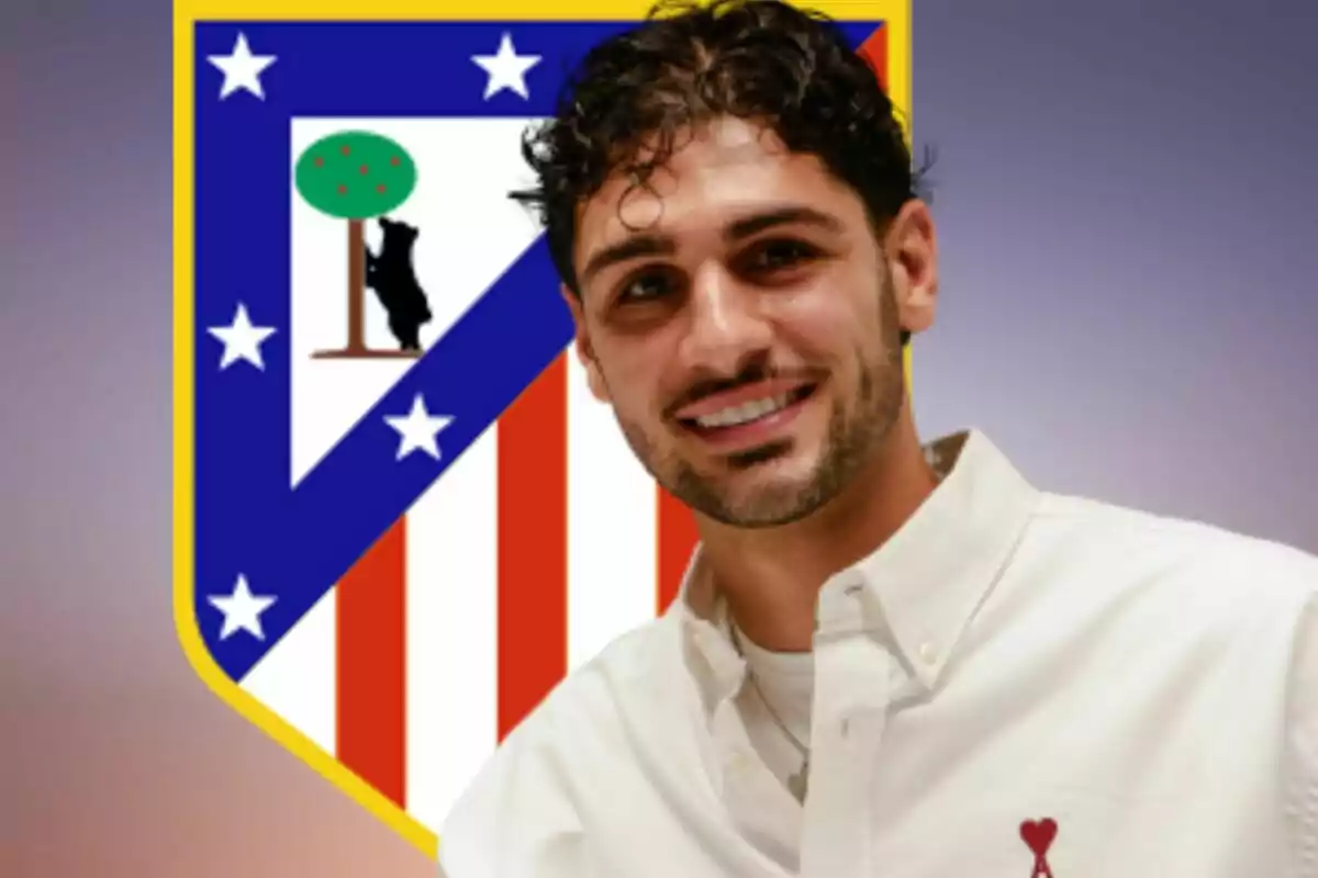 Hombre sonriente con camisa blanca posando frente al escudo del Atlético de Madrid