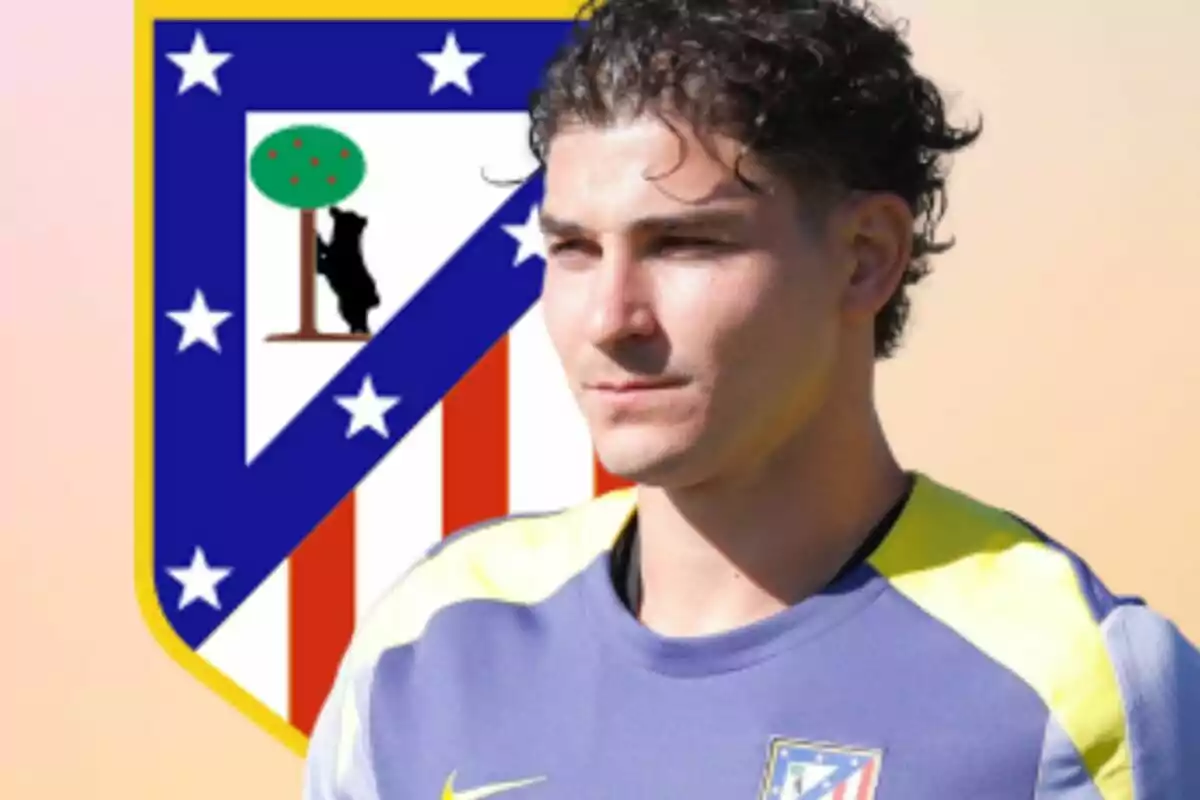 Jugador de fútbol con uniforme de entrenamiento del Atlético de Madrid posando frente al escudo del club