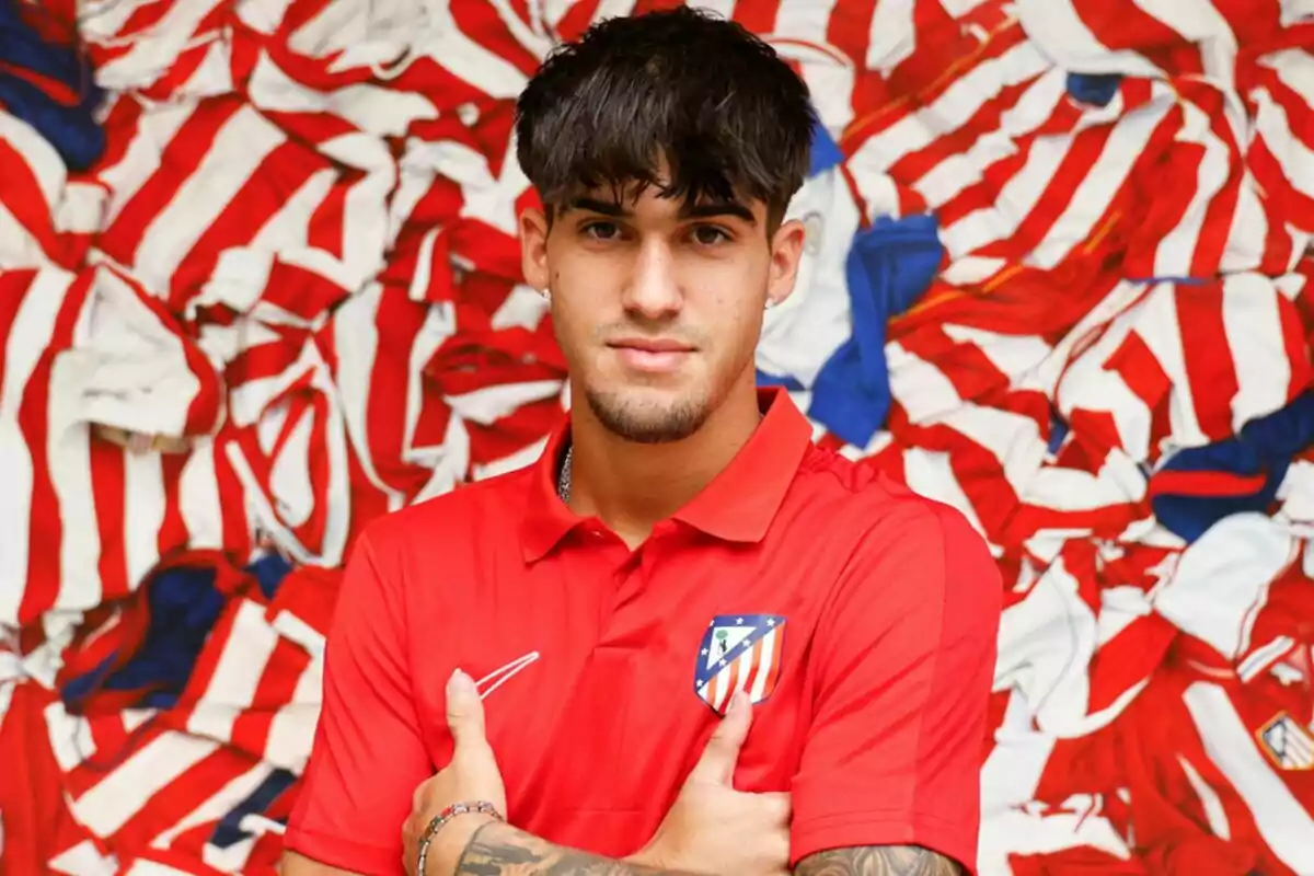 Joven con camiseta roja del Atlético de Madrid posando frente a un fondo de camisetas rojiblancas Joven con camiseta roja del Atlético de Madrid posando frente a un fondo de camisetas rojiblancas