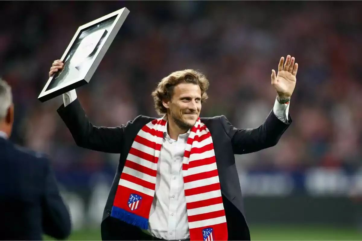 Hombre con bufanda del Atlético de Madrid levantando un cuadro y saludando en un estadio lleno de gente Hombre con bufanda del Atlético de Madrid levantando un cuadro y saludando en un estadio lleno de gente
