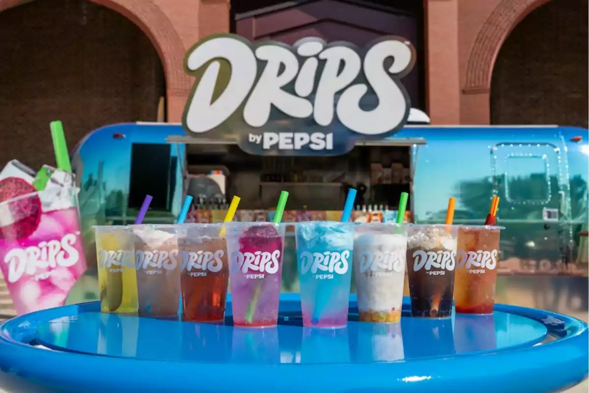 Colorful Drips by Pepsi drink cups with straws of different colors on a blue table in front of a decorated trailer and a large Drips sign Colorful Drips by Pepsi drink cups with straws of different colors on a blue table in front of a decorated trailer and a large Drips sign