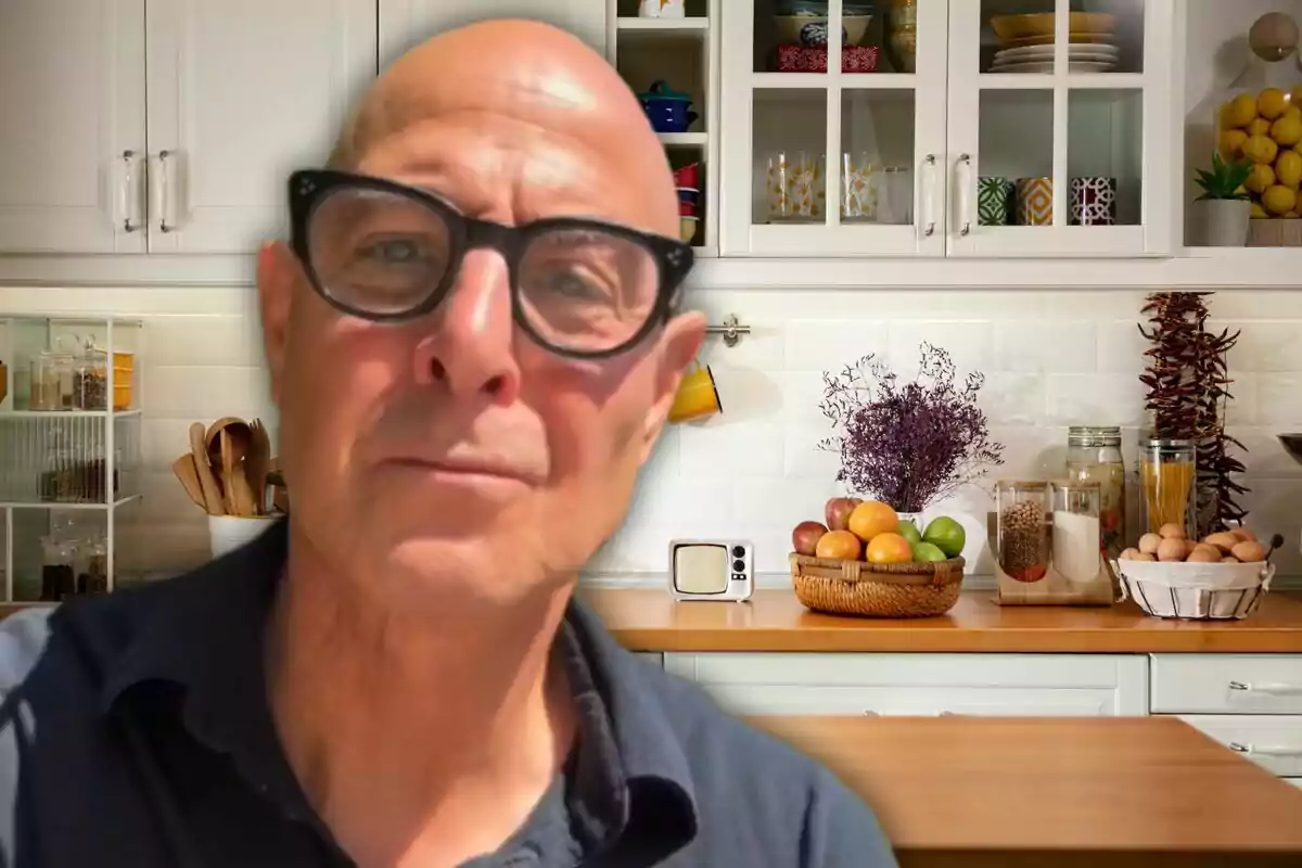 Hombre calvo con gafas oscuras en primer plano dentro de una cocina moderna con frutas y utensilios sobre la encimera