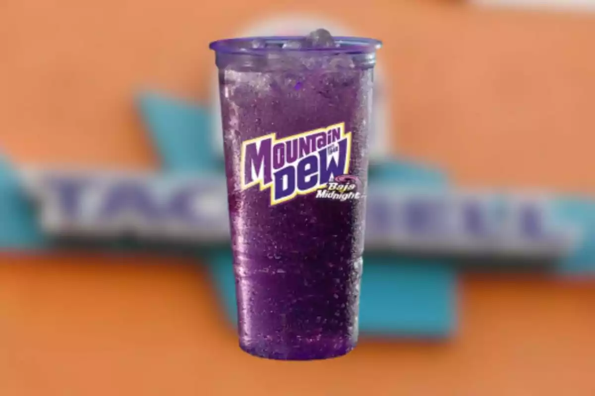 Vaso transparente con bebida morada Mountain Dew Baja Midnight con hielo y fondo desenfocado de colores naranja y azul