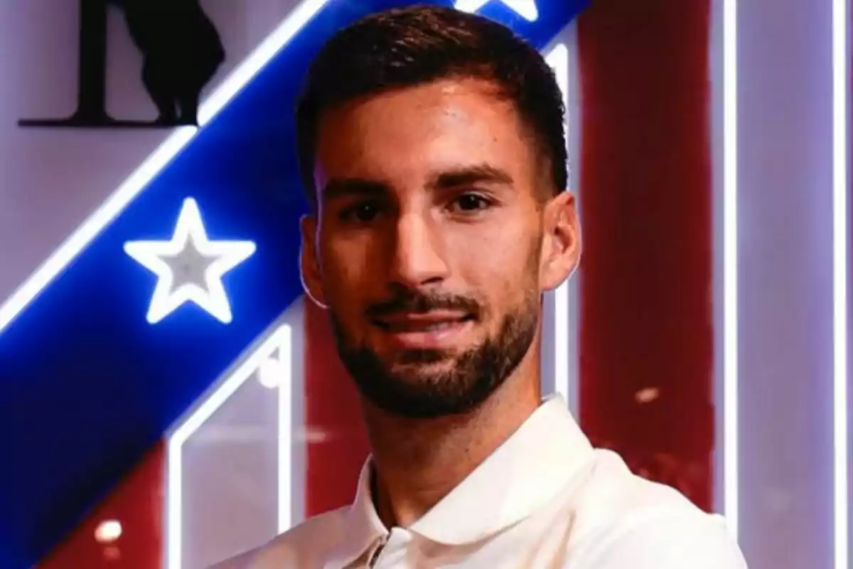 Hombre joven con barba y cabello corto posando frente a un fondo con los colores y símbolos del Atlético de Madrid
