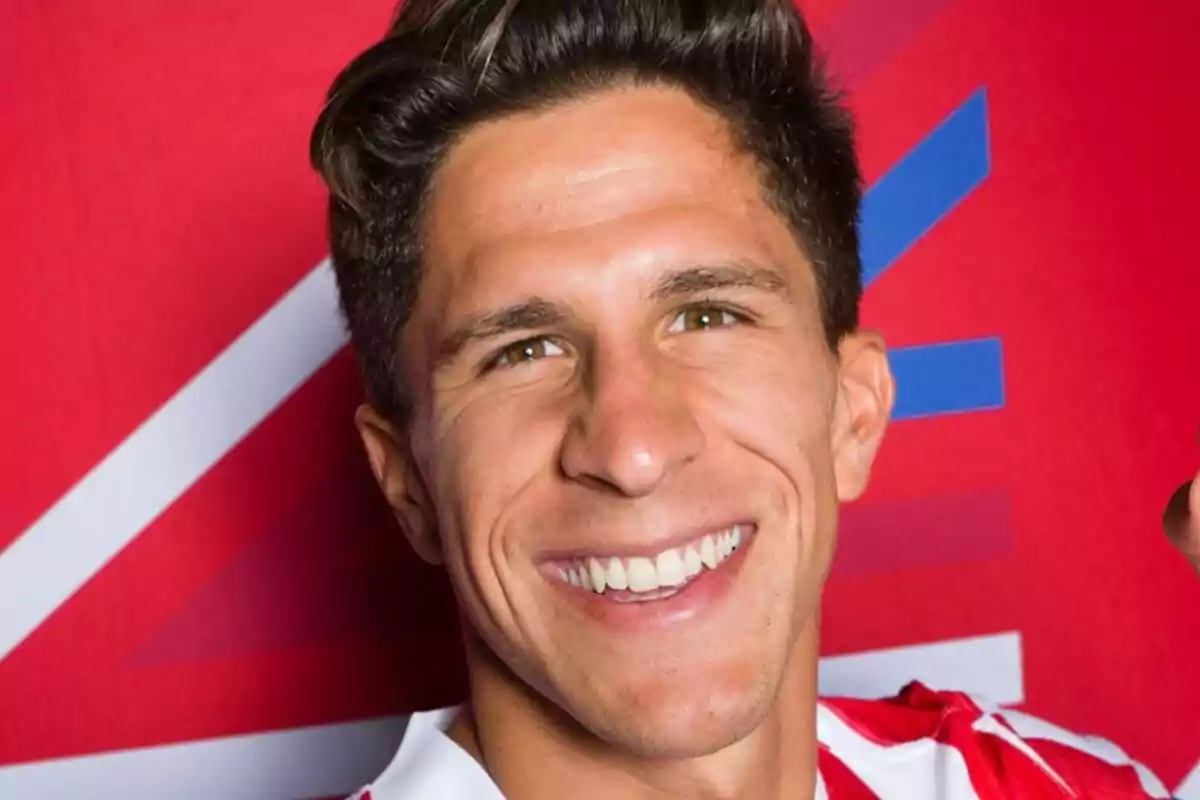 Joven sonriente con camiseta de rayas rojas y blancas frente a un fondo rojo con detalles geométricos azules y blancos