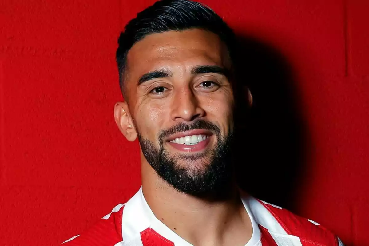 Hombre con barba y cabello corto sonriendo, vistiendo una camiseta roja con blanco y fondo rojo