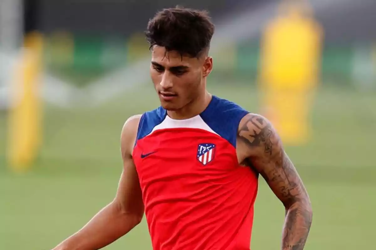 Jugador de fútbol con camiseta de entrenamiento roja del Atlético de Madrid en el campo.