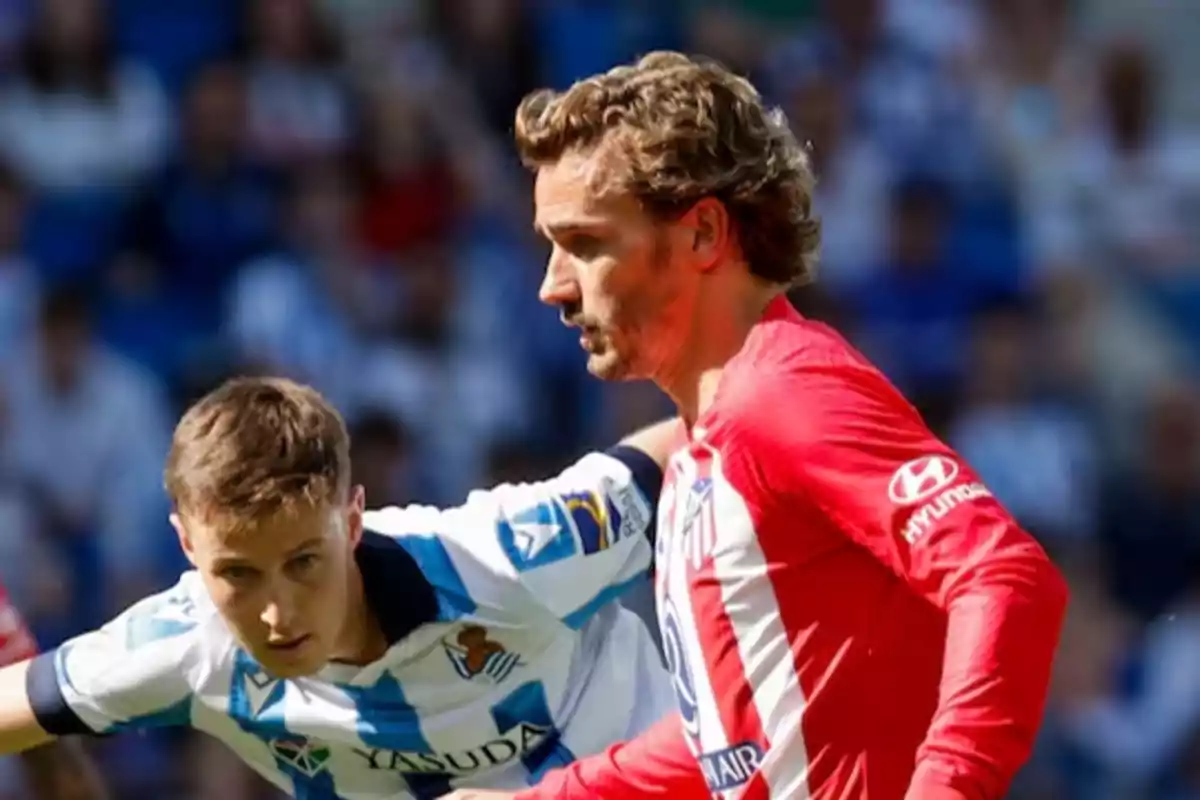 Dos jugadores de fútbol en acción durante un partido uno con uniforme rojo y el otro con uniforme blanco y azul.