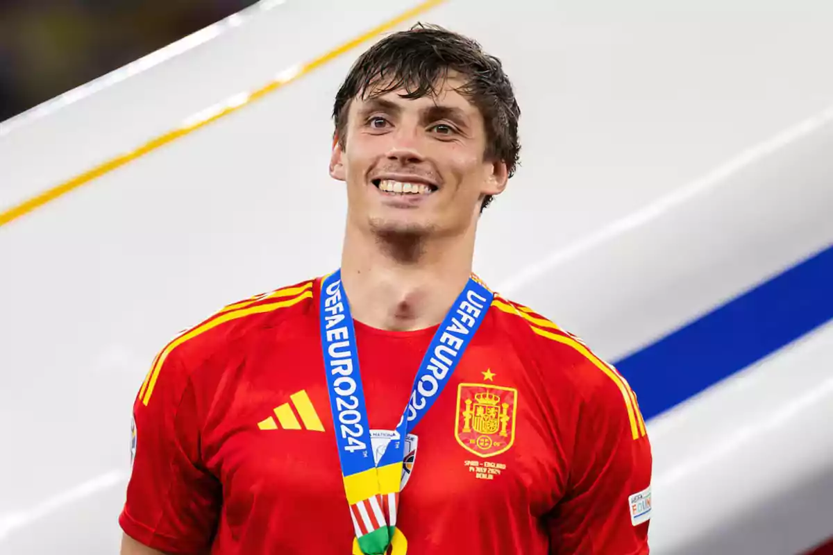 Jugador de fútbol con la camiseta de la selección española y una medalla de la UEFA Euro 2024 sonríe frente a la cámara.