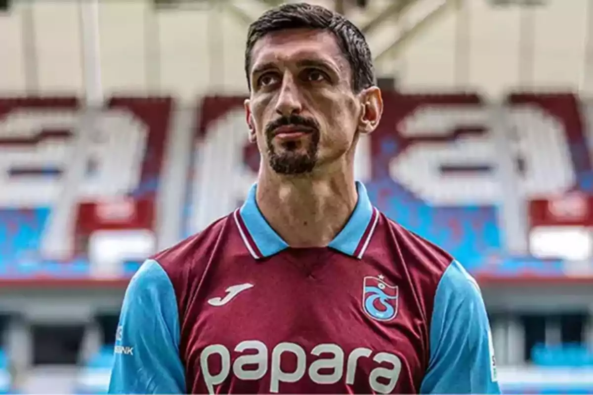 Jugador de fútbol con uniforme granate y celeste en un estadio.