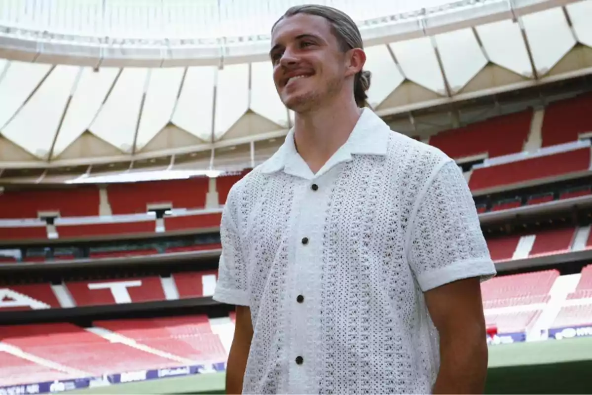 Un hombre con una camisa blanca de encaje está de pie en un estadio de fútbol vacío.