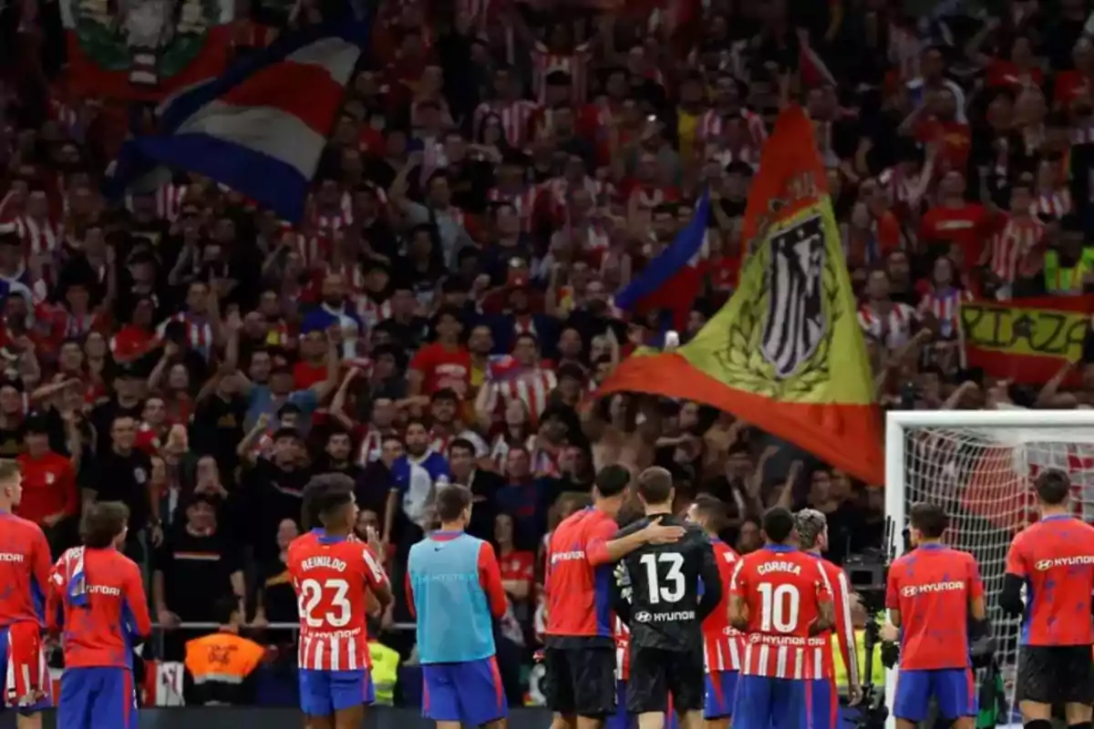 Atlético de Madrid football players in front of a crowd of fans at the stadium, with red and white flags and shirts.