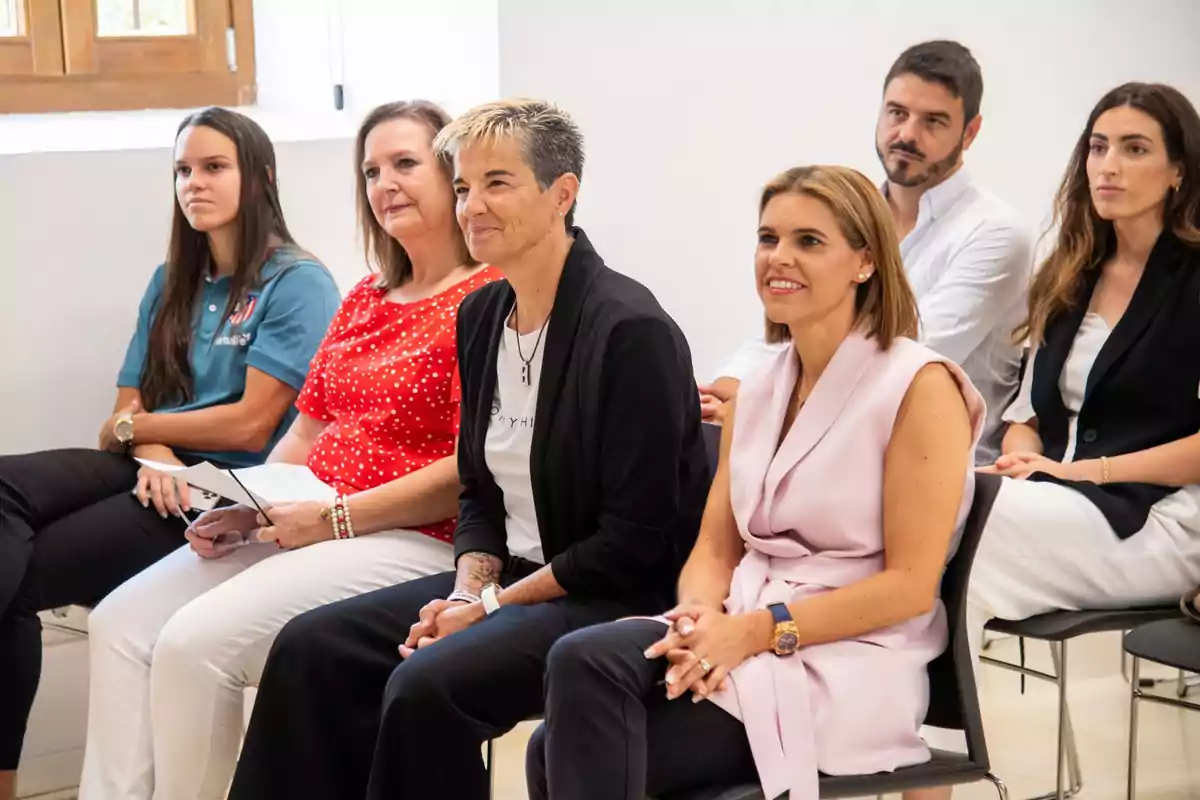 Un grupo de personas sentadas en una sala, prestando atención a algo fuera de la imagen.