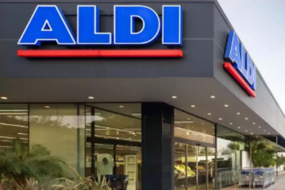 Fachada de una tienda con el logotipo de ALDI en letras grandes y azules sobre un fondo gris. Fachada de una tienda con el logotipo de ALDI en letras grandes y azules sobre un fondo gris.