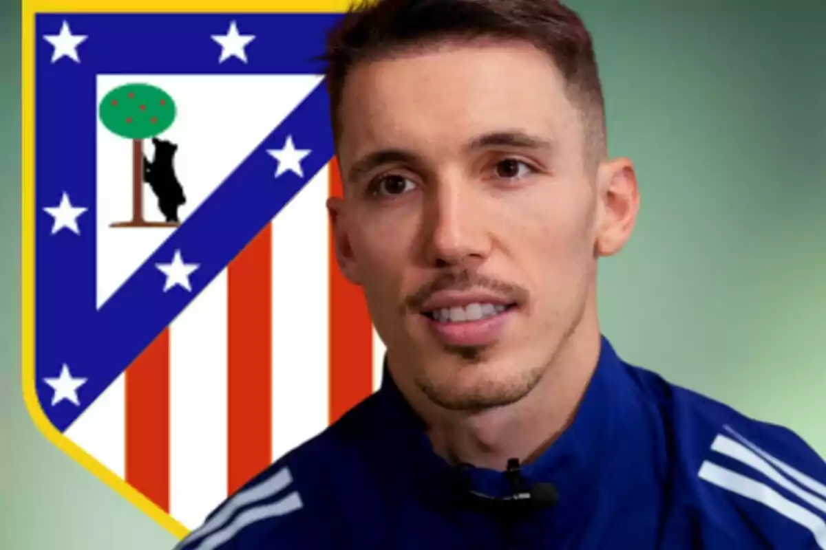 Un hombre con chaqueta deportiva azul está frente al escudo del Atlético de Madrid