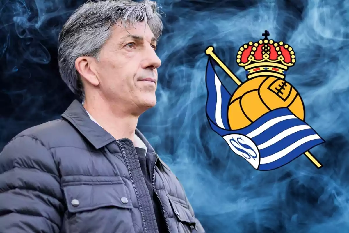 Hombre de cabello canoso con chaqueta negra frente al escudo de la Real Sociedad sobre un fondo de humo azul.