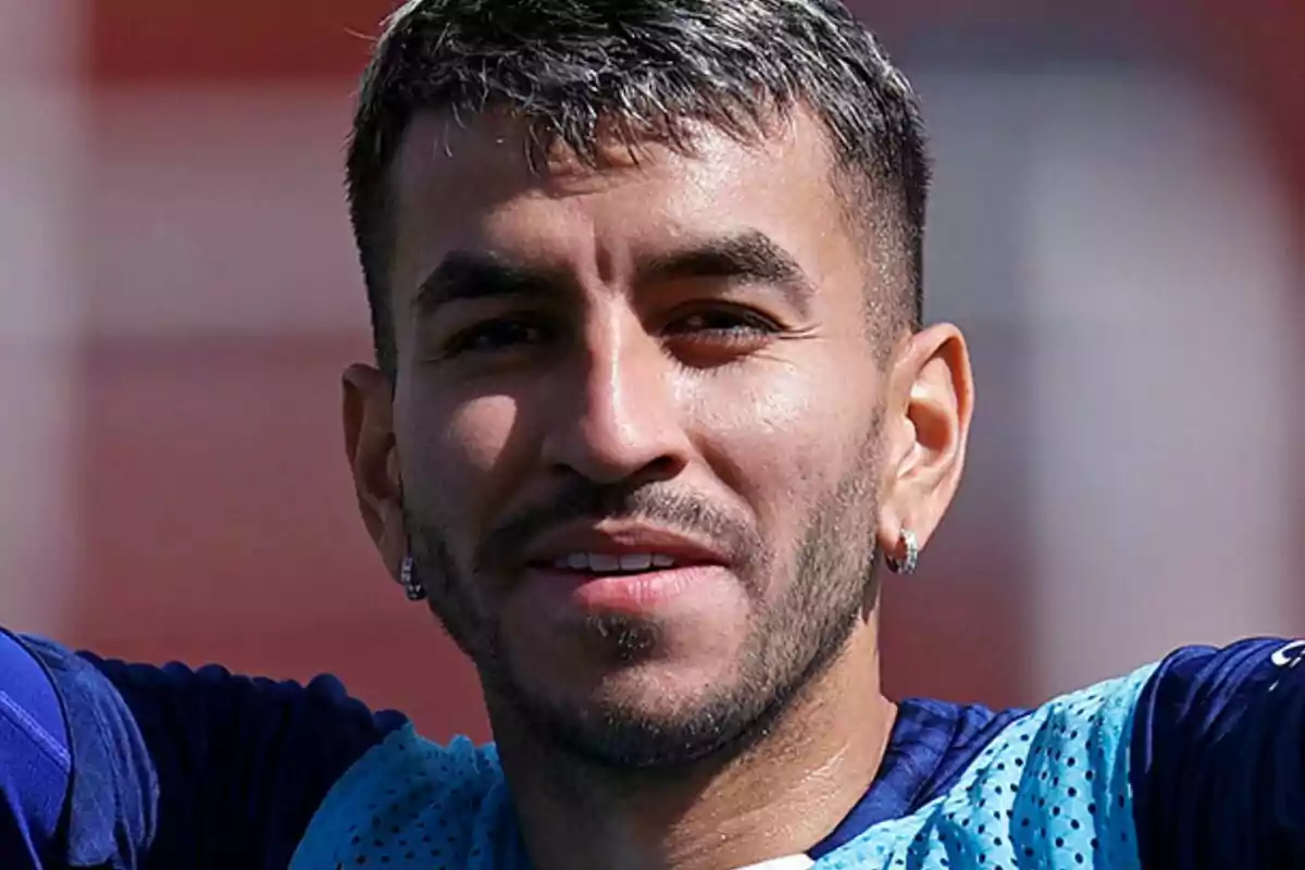 Un hombre con barba y cabello corto sonríe mientras lleva una camiseta deportiva azul.
