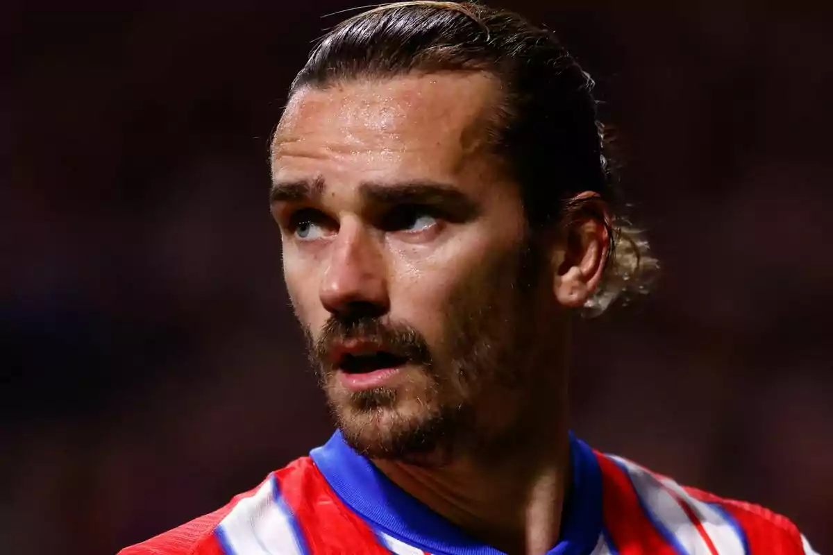 Un jugador de fútbol con camiseta roja y azul mira hacia un lado en un estadio.