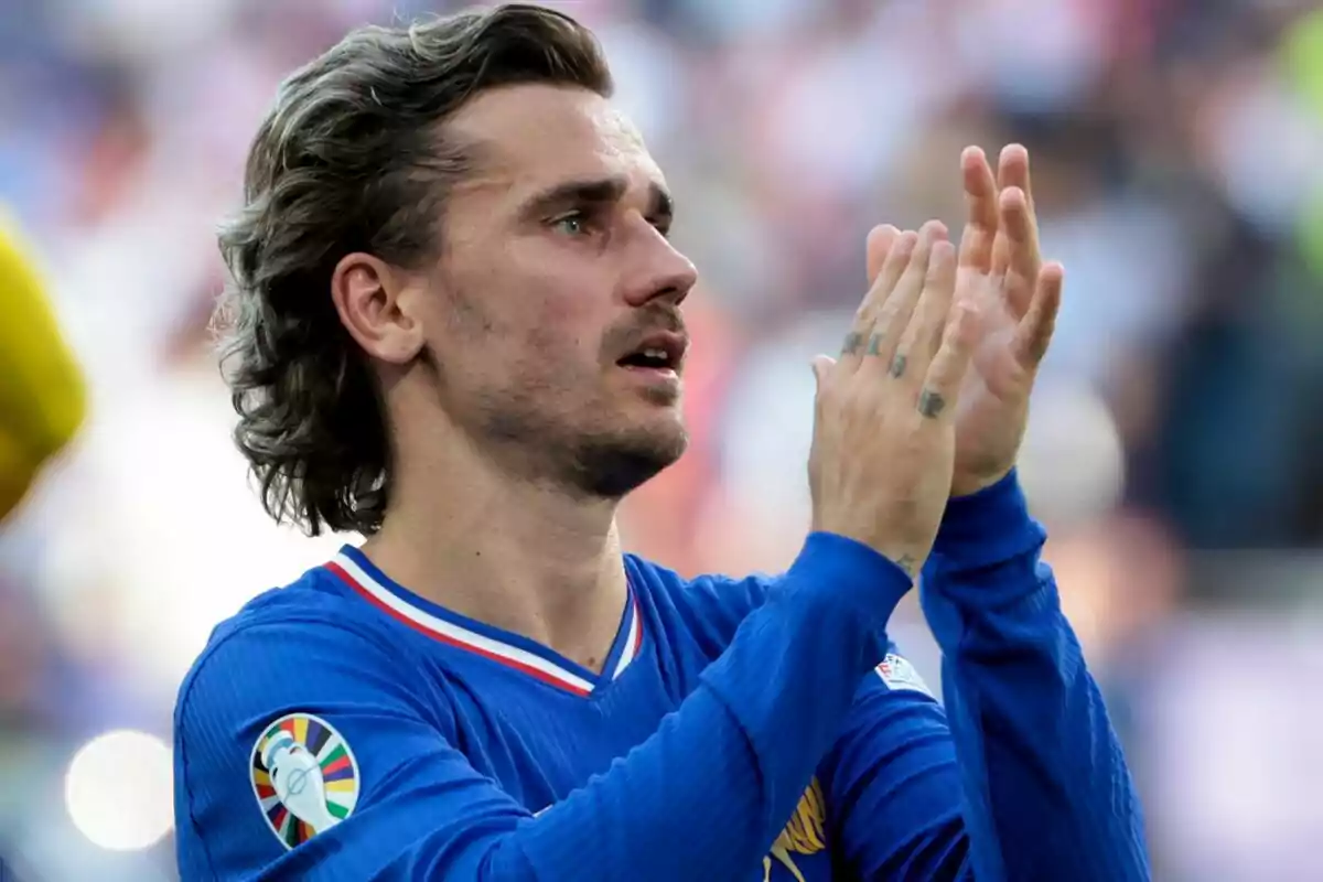 Un jugador de fútbol con uniforme azul aplaudiendo en un estadio.