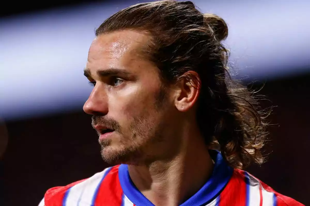 A player with long hair and a beard looks to the side while wearing a red and white striped jersey.